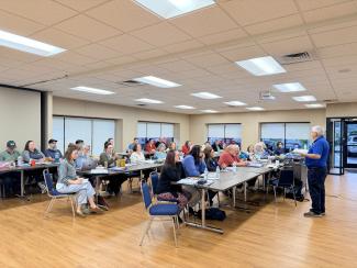 a group of people sitting in a classroom style setting listening to a speaker